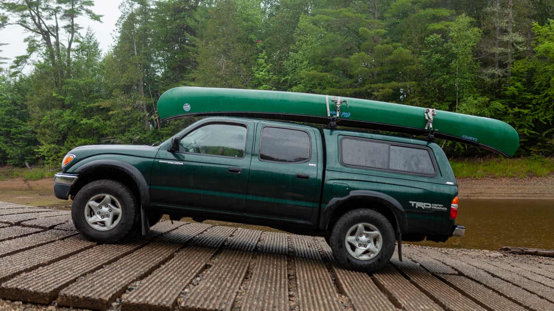 Green Toyota Tacoma on a boat launch with canoe on roof rack.